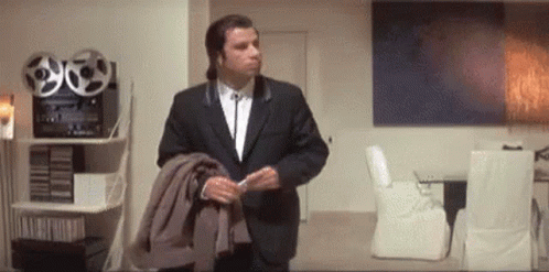 A Man In A Suit And Tie Is Standing In A Living Room Holding His Jacket . GIF