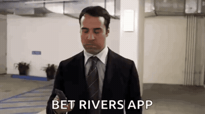 A Man In A Suit And Tie Is Standing In A Parking Garage And Looking At His Phone . GIF