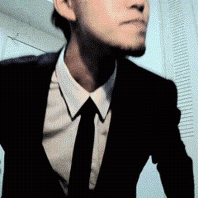 A Man In A Suit And Tie Is Standing In A Room GIF