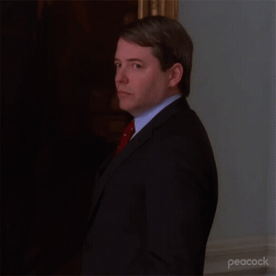 A Man In A Suit And Tie Is Standing In A Room . GIF