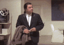 A Man In A Suit And Tie Is Standing In A Room Holding A Coat . GIF