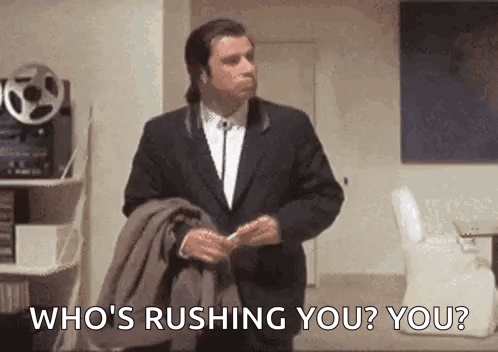 A Man In A Suit And Tie Is Standing In A Room Holding A Jacket And Asking Who 'S Rushing You ? GIF