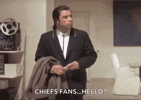 A Man In A Suit And Tie Is Standing In A Room Holding A Jacket And Talking To A Fan . GIF