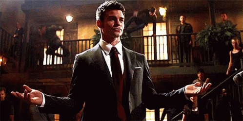 A Man In A Suit And Tie Is Standing In A Room With His Arms Outstretched GIF