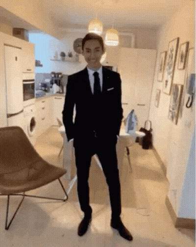 A Man In A Suit And Tie Is Standing In A Room With His Hands In His Pockets . GIF