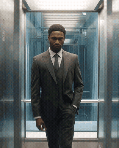 A Man In A Suit And Tie Is Standing In An Elevator With His Hands In His Pockets GIF