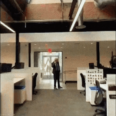 A Man In A Suit And Tie Is Standing In An Office Talking On His Cell Phone . GIF