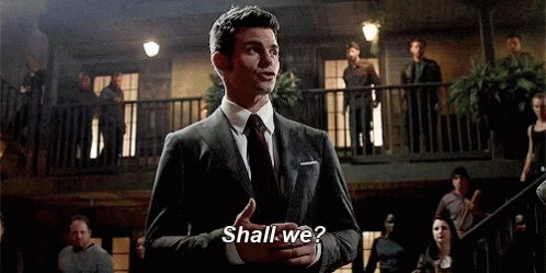 A Man In A Suit And Tie Is Standing In Front Of A Balcony Talking To A Crowd . GIF