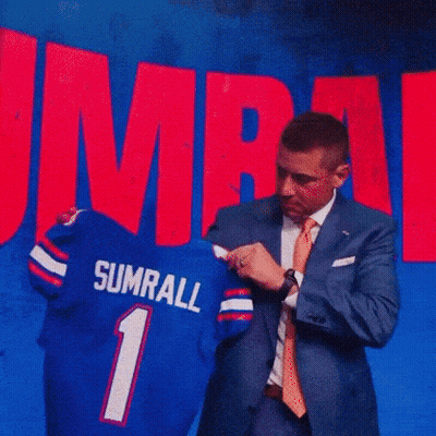 A Man In A Suit And Tie Is Standing In Front Of A Banner That Says Ump GIF