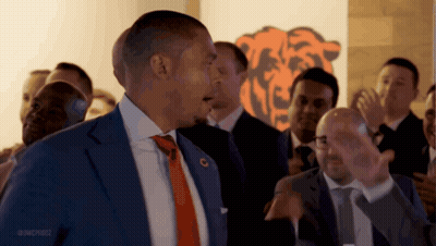 A Man In A Suit And Tie Is Standing In Front Of A Bears Logo GIF