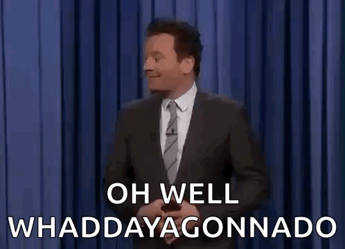 A Man In A Suit And Tie Is Standing In Front Of A Blue Curtain And Saying Oh Well Whaddayagonnado . GIF