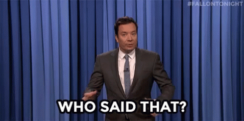 A Man In A Suit And Tie Is Standing In Front Of A Blue Curtain And Saying `` Who Said That ? '' GIF