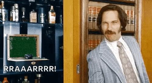 A Man In A Suit And Tie Is Standing In Front Of A Bookshelf With Bottles Of Alcohol . GIF