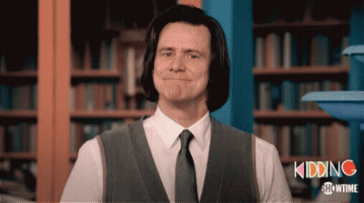 A Man In A Suit And Tie Is Standing In Front Of A Bookshelf With The Words Kidding Showtime On The Bottom GIF