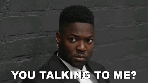 A Man In A Suit And Tie Is Standing In Front Of A Brick Wall And Saying `` You Talking To Me ? '' GIF