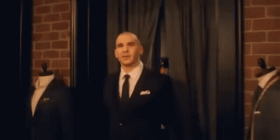A Man In A Suit And Tie Is Standing In Front Of A Brick Wall In A Room . GIF