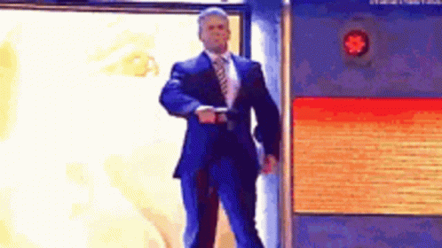 A Man In A Suit And Tie Is Standing In Front Of A Brick Wall . GIF