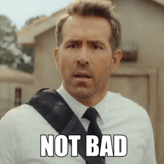 A Man In A Suit And Tie Is Standing In Front Of A Building . GIF