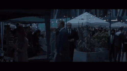 A Man In A Suit And Tie Is Standing In Front Of A Building And Says Let The Games Begin . GIF