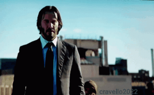 A Man In A Suit And Tie Is Standing In Front Of A Building That Says Cravello2022 On It GIF