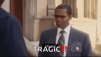 A Man In A Suit And Tie Is Standing In Front Of A Building With The Word Tragic Written On The Bottom Of The Screen . GIF