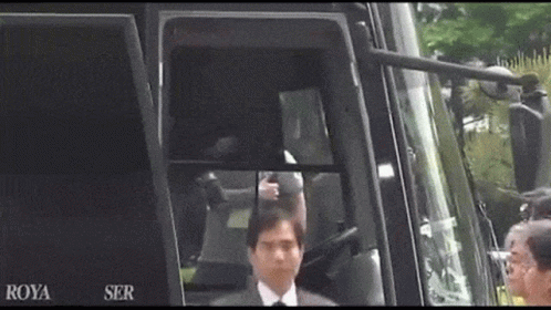 A Man In A Suit And Tie Is Standing In Front Of A Bus That Says Roya Ser On It GIF