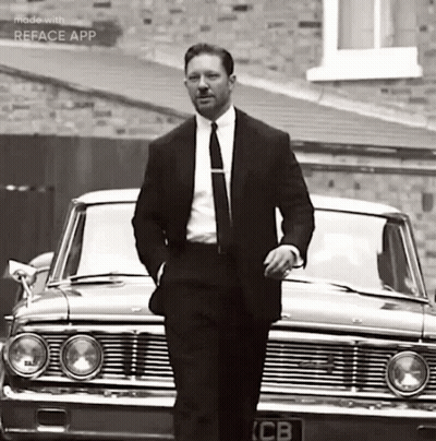 A Man In A Suit And Tie Is Standing In Front Of A Car . GIF