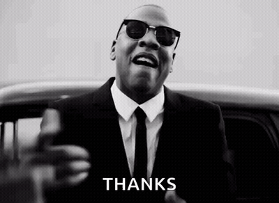 A Man In A Suit And Tie Is Standing In Front Of A Car And Giving A Thanks Sign . GIF