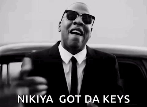 A Man In A Suit And Tie Is Standing In Front Of A Car And Holding A Gun . GIF