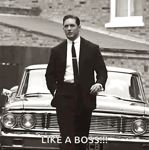 A Man In A Suit And Tie Is Standing In Front Of A Car In A Black And White Photo . GIF
