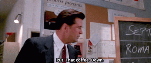 A Man In A Suit And Tie Is Standing In Front Of A Chalkboard That Says " Put That Coffee Down " GIF
