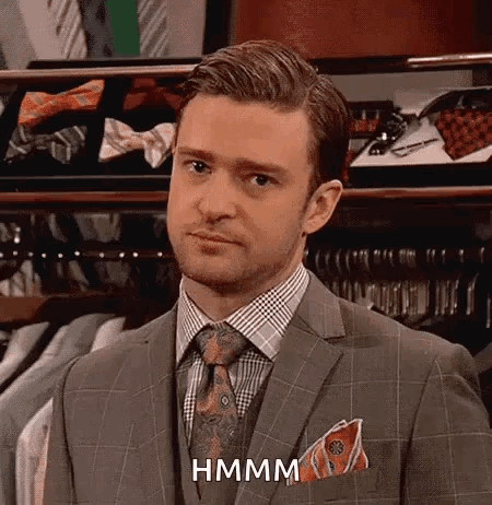 A Man In A Suit And Tie Is Standing In Front Of A Closet Filled With Shirts And Ties . GIF