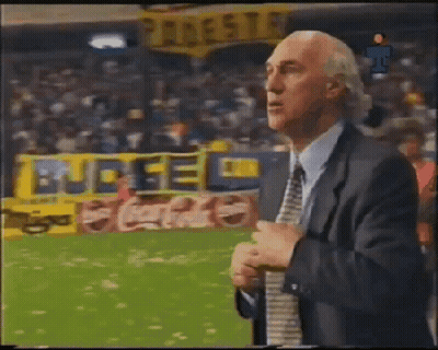A Man In A Suit And Tie Is Standing In Front Of A Coca Cola Banner GIF
