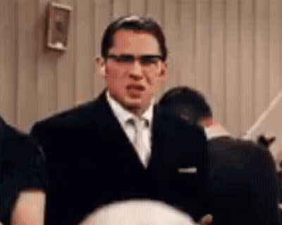 A Man In A Suit And Tie Is Standing In Front Of A Crowd . GIF