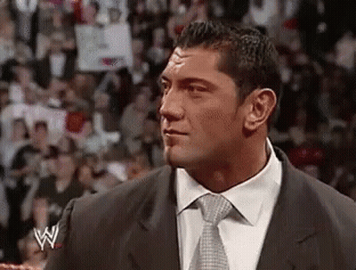 A Man In A Suit And Tie Is Standing In Front Of A Crowd In A Ring . GIF
