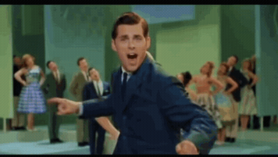 A Man In A Suit And Tie Is Standing In Front Of A Crowd Of People . GIF