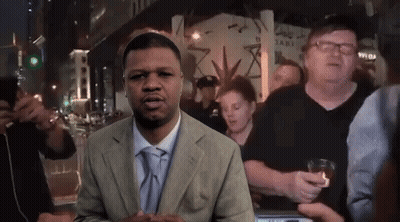 A Man In A Suit And Tie Is Standing In Front Of A Crowd Of People GIF