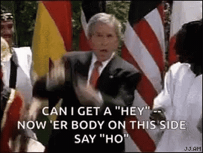 A Man In A Suit And Tie Is Standing In Front Of A Crowd Of People And Flags . GIF