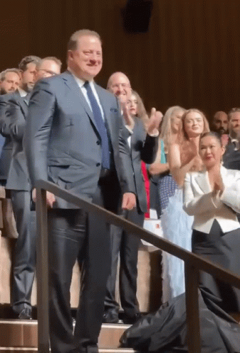 A Man In A Suit And Tie Is Standing In Front Of A Crowd Of People GIF