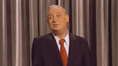 A Man In A Suit And Tie Is Standing In Front Of A Curtain And Making A Funny Face . GIF