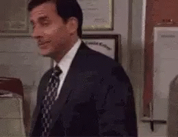 A Man In A Suit And Tie Is Standing In Front Of A Door In An Office . GIF