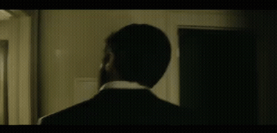 A Man In A Suit And Tie Is Standing In Front Of A Door . GIF