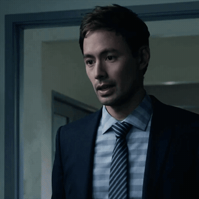 A Man In A Suit And Tie Is Standing In Front Of A Door GIF