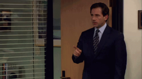 A Man In A Suit And Tie Is Standing In Front Of A Door With Blinds On It . GIF