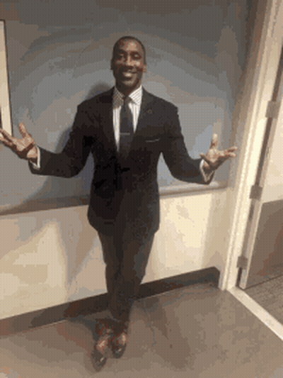 A Man In A Suit And Tie Is Standing In Front Of A Door With His Arms Outstretched GIF