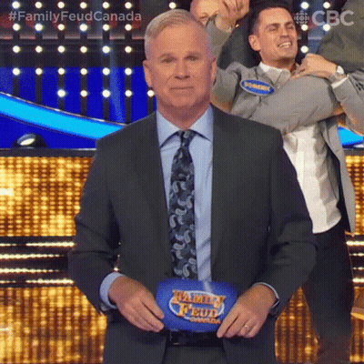 A Man In A Suit And Tie Is Standing In Front Of A Family Feud Podium . GIF