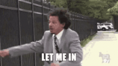 A Man In A Suit And Tie Is Standing In Front Of A Fence And Says `` Let Me In '' . GIF