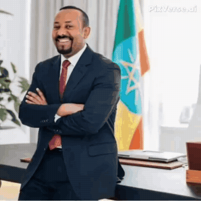 A Man In A Suit And Tie Is Standing In Front Of A Flag With His Arms Crossed And Smiling . GIF