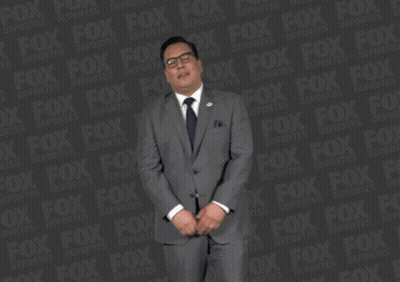 A Man In A Suit And Tie Is Standing In Front Of A Fox Logo GIF