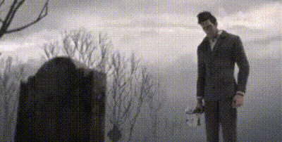 A Man In A Suit And Tie Is Standing In Front Of A Grave In A Cemetery . GIF